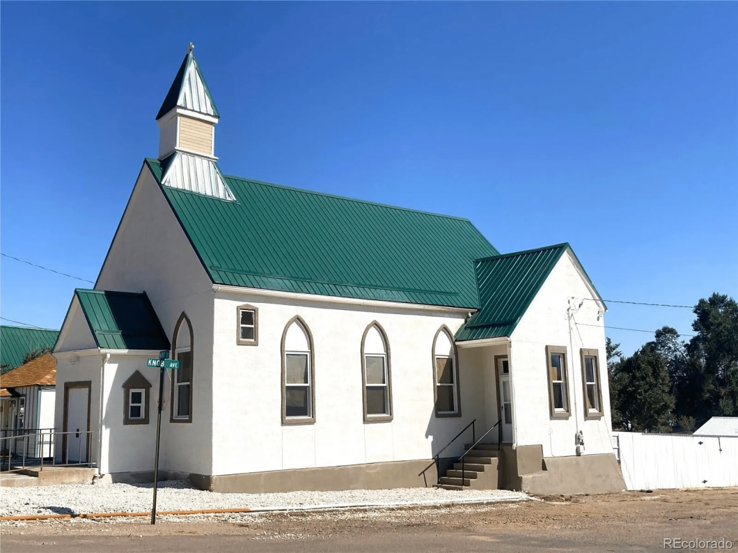 Side angle of a church building with tall, arched windows and a green metal roof.