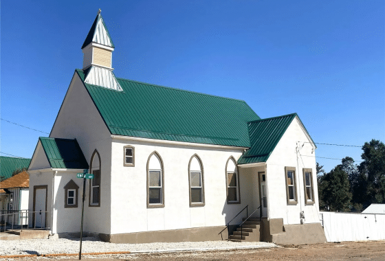 Side angle of a church building with tall, arched windows and a green metal roof.